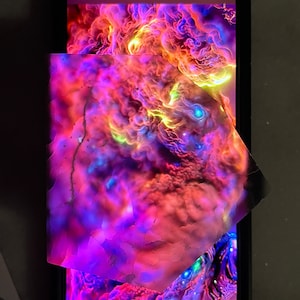 K&ouml;nnte beinhalten: Nahaufnahme eines Smartphone-Bildschirms, der ein farbenfrohes abstraktes Bild mit wirbelnden Mustern in Rosa-, Lila-, Orange- und Gelbt&ouml;nen zeigt. Das Bild wird teilweise von einem St&uuml;ck durchscheinendem Material mit einem &auml;hnlichen abstrakten Muster verdeckt.