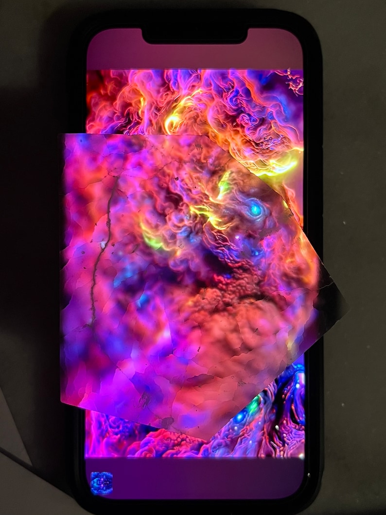 K&ouml;nnte beinhalten: Nahaufnahme eines Smartphone-Bildschirms, der ein farbenfrohes abstraktes Bild mit wirbelnden Mustern in Rosa-, Lila-, Orange- und Gelbt&ouml;nen zeigt. Das Bild wird teilweise von einem St&uuml;ck durchscheinendem Material mit einem &auml;hnlichen abstrakten Muster verdeckt.