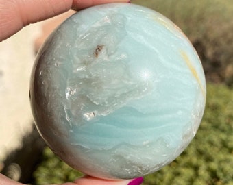 May include: A light blue and white agate sphere with brown and white inclusions. The sphere is smooth and polished.