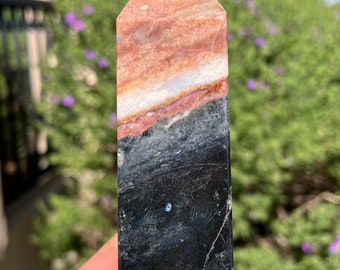 Puede incluir: Una punta de cristal rayada de negro y rosa con una punta puntiaguda. El cristal está pulido y tiene una superficie lisa.