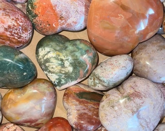 May include: A collection of heart-shaped polished stones in various shades of brown, pink, green, and white. The stones have a natural, marbled pattern.