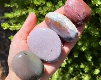 Può includere: Quattro pietre lisce e levigate in varie tonalità di viola, marrone e verde. Le pietre sono disposte in una pila, con la pietra più grande in basso e la più piccola in alto.