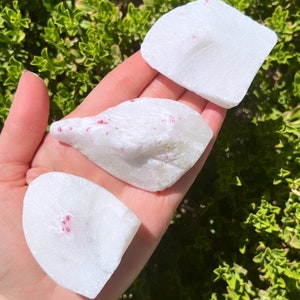 Op de afbeelding: Drie witte, ruwe, onregelmatig gevormde stenen met kleine rode robijn-insluitsels.