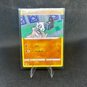 May include: A Pok&eacute;mon trading card featuring Cubone, with a yellow and orange design. The card shows an illustration of the Cubone character holding a bone. The card includes the text "Cubone", "Beat", and "Headbutt".