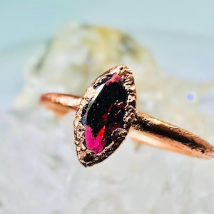 May include: A copper ring with a marquise-shaped, deep red gemstone set in the band.