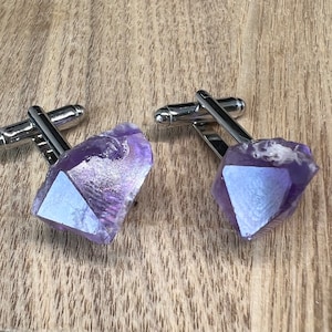 May include: A pair of silver cufflinks with amethyst crystal accents. The crystals are a deep purple color and have a faceted, geometric shape.