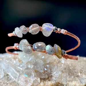 May include: A copper wire bracelet with labradorite stones. The bracelet is wrapped around a cluster of clear quartz crystals.
