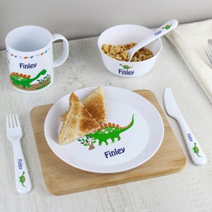May include: A white personalised children's dinosaur themed dinner set with a plate, bowl, mug, fork and knife. The set features a green dinosaur with orange accents and the name "Finley" printed on each piece.