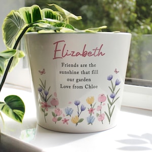 May include: Cream ceramic plant pot with a floral design and the name "Elizabeth" in pink script. The pot has a message that reads "Friends are the sunshine that fill our garden Love from Chloe."