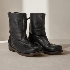 May include: A pair of black leather ankle boots. The boots have a worn, distressed appearance with a low heel and a strap detail around the ankle. The leather is creased, and the soles show wear.