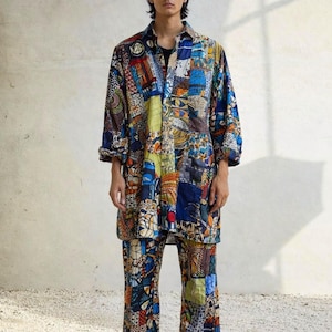 May include: A colourful patchwork shirt and trousers set. The long-sleeved shirt has a collared neckline and the trousers are wide-legged. The outfit features a mix of blue, yellow, and red patches. The outfit is worn with black shoes.
