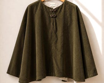 May include: An olive green corduroy cape featuring a round neckline, two dark circular toggle closures at the collar, and a light-colored patterned lining. The garment is displayed on a wooden hanger against a neutral background.