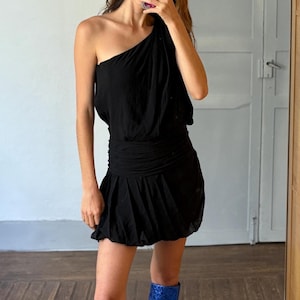 May include: A black one-shoulder dress with a gathered waist and a short, bubble hem. The dress is paired with knee-high, blue, sparkly boots with block heels. The outfit is reflected in a mirror.
