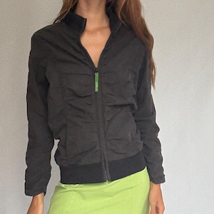 May include: Black zip-up jacket with a high collar and a lime green mini skirt. The jacket has a green zipper pull. The model is wearing blue knee-high boots.