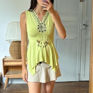 Peut inclure: Un haut sans manches vert citron avec un décolleté en V orné de broderies perlées complexes et de franges pendantes, associé à une mini-jupe beige et des bottes hautes en daim marron. Le haut présente un ourlet évasé et un corsage ajusté.