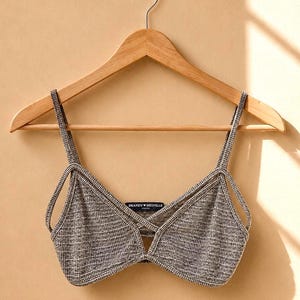 May include: A black and white textured knit bralette featuring thin shoulder straps, a V-neckline with a crisscross detail at the center, and a Brandy Melville label sewn into the inner neckline, all displayed on a wooden clothes hanger.