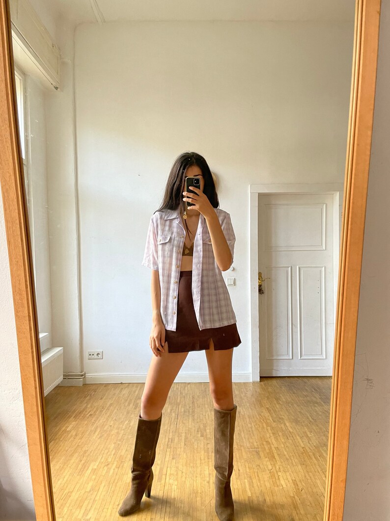 May include: A woman wearing a white and pink plaid shirt, a brown mini skirt with a slit, and brown knee-high boots.