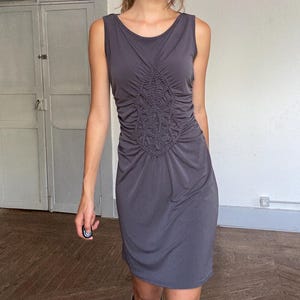 Pode incluir: Um vestido sem mangas cinza carvão com decote redondo. O vestido apresenta detalhes intrincados de franzidos e franzidos no corpete, criando um design texturizado e atraente. O vestido é na altura do joelho e é feito de um tecido macio e fluido.