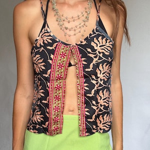 Könnte beinhalten: Schwarzes Camisole-Top mit orangefarbenem Blumenmuster und Schlüsselloch-Design. Das Top hat dünne Träger und eine dekorative rot-goldene Bordüre. Eine mehrsträngige Perlenkette wird mit dem Top getragen. Das Model trägt einen limettengrünen Rock.