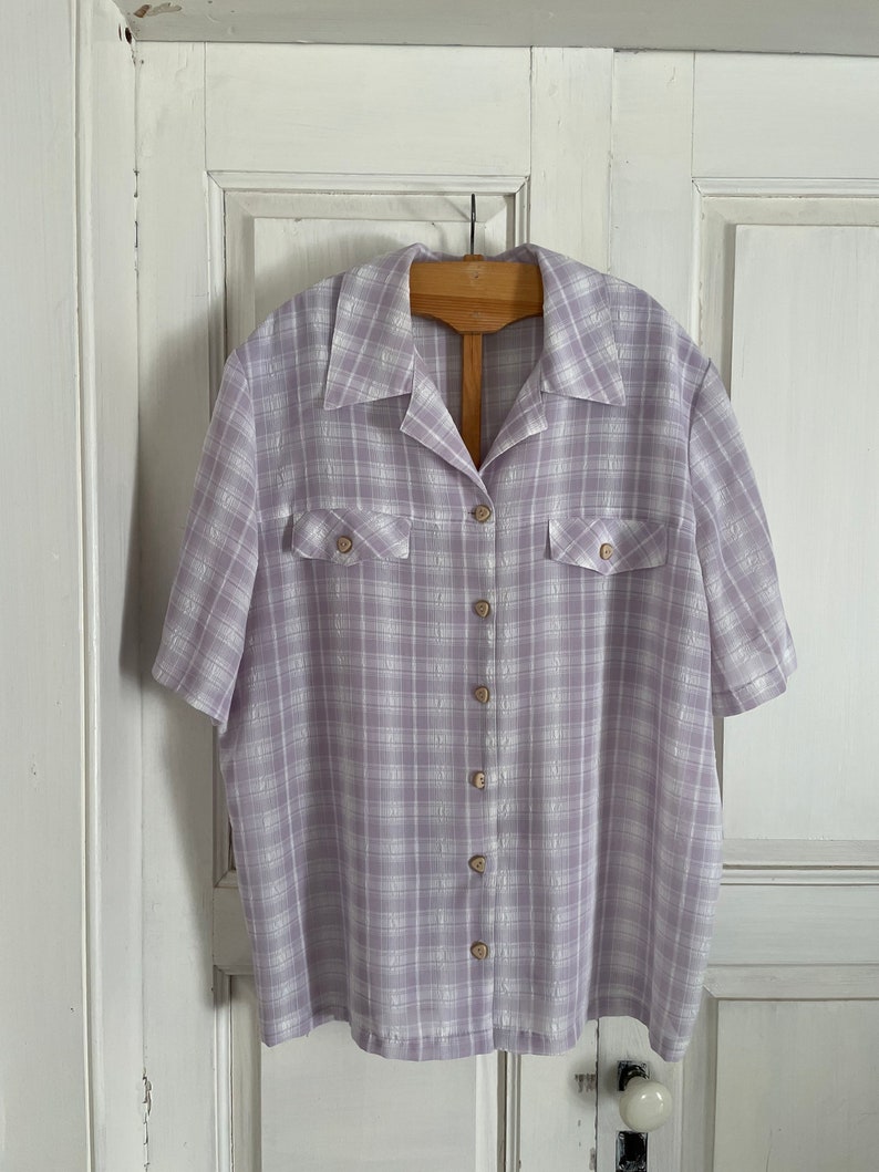 May include: A lavender and white plaid button-up shirt with short sleeves and two chest pockets.