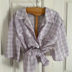 May include: A lavender and white plaid button-up shirt with short sleeves. The shirt is tied at the waist.