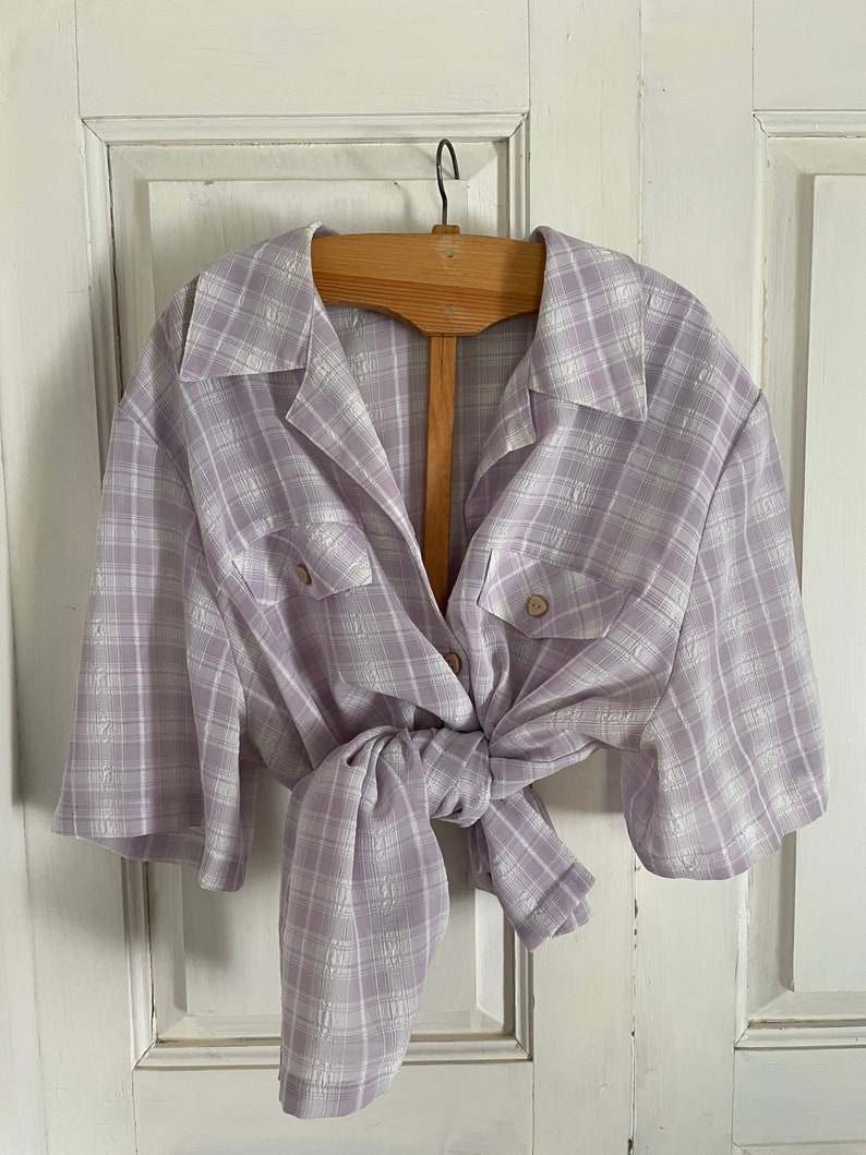 May include: A lavender and white plaid button-up shirt with short sleeves. The shirt is tied at the waist.