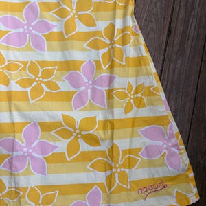 May include: A yellow and white striped dress with a floral pattern of pink and yellow flowers. The dress has a pink trim at the top and the Rip Curl logo near the bottom.
