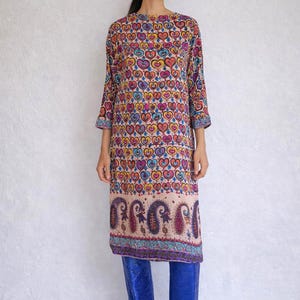 Puede incluir: Vestido largo hasta la rodilla con estampado de corazones multicolores sobre fondo beige. Borde con diseño de cachemir. La persona lleva botas azules.