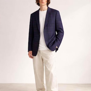 Può includere: Un blazer blu navy a quadri, abbinato a una t-shirt bianca e pantaloni color crema. Il blazer presenta un motivo sottile. L'outfit è adatto per un look casual elegante.