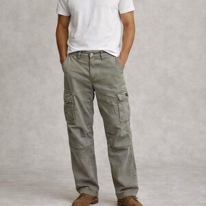Pode incluir: Uma pessoa vestindo uma camiseta branca de gola redonda e calças cargo verde-oliva com vários bolsos. A pessoa também está usando sapatos de couro marrom. A roupa é casual e adequada para o uso diário.