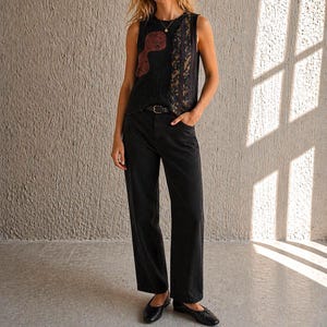 May include: A black sleeveless top with a red and brown abstract design, worn with black jeans and black flats. The top has a textured appearance and a decorative panel on the side. A thin black belt is worn with the jeans.