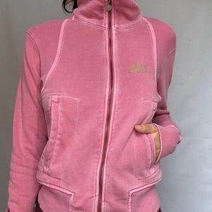 K&ouml;nnte beinhalten: Rosa Rei&szlig;verschlussjacke mit hohem Kragen und langen &Auml;rmeln. Die Jacke hat einen Frontrei&szlig;verschluss, Taschen und ein kleines Logo auf der Brust. Die Jacke ist aus einem weichen, strukturierten Material.