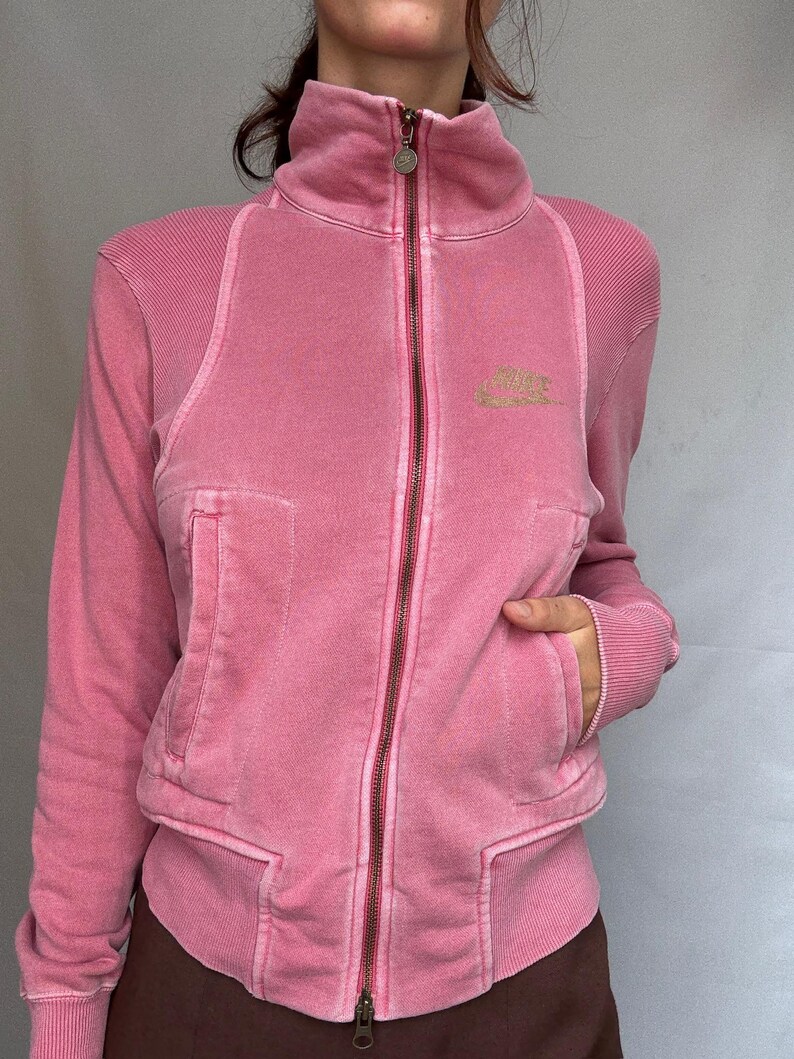 K&ouml;nnte beinhalten: Rosa Rei&szlig;verschlussjacke mit hohem Kragen und langen &Auml;rmeln. Die Jacke hat einen Frontrei&szlig;verschluss, Taschen und ein kleines Logo auf der Brust. Die Jacke ist aus einem weichen, strukturierten Material.