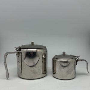 Könnte beinhalten: Zwei Teekannen aus Edelstahl mit Deckel und Griffen. Die größere Teekanne hat ein Fassungsvermögen von etwa 1,2 Litern, während die kleinere etwa 0,6 Liter fasst. Beide haben eine glänzende, reflektierende Oberfläche.