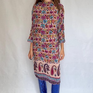 Puede incluir: Vestido hasta la rodilla con un estampado de corazones en tonos rosa, amarillo, azul y morado. El vestido tiene mangas largas y un borde de cachemira. La persona lleva botas azules.