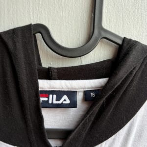 May include: A white and black hooded sweatshirt with the brand name "FILA" in white letters on a navy blue label with a red stripe. The size "16" is printed on a separate label.