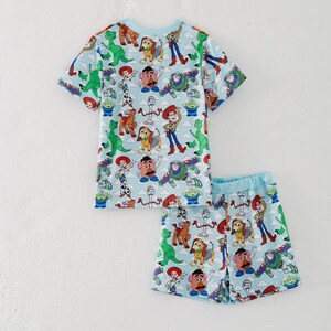 K&ouml;nnte beinhalten: Ein hellblaues zweiteiliges Pyjama-Set mit einem farbenfrohen Aufdruck von Toy Story-Charakteren. Das Set enth&auml;lt ein kurz&auml;rmeliges Oberteil und passende Shorts. Das Oberteil und die Shorts haben einen hellblauen Besatz.