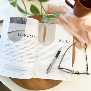 Puede incluir: Primer plano de un libro abierto con los títulos "Fragrance" y "Wicks" en las páginas. El libro está abierto en una página sobre la fabricación de velas e incluye información sobre notas de fragancia y tamaños de mechas. Un bolígrafo y unas gafas están sobre el libro.