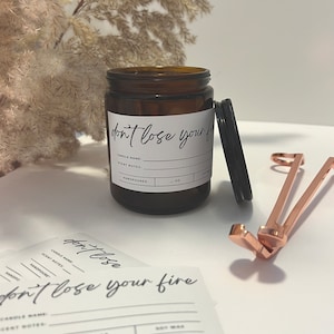 May include: A brown glass candle jar with a white label that says "don't lose your fire". The label also includes the words "candle name", "scent notes", and "handpoured".
