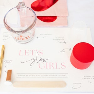 May include: Candle-making kit with a measuring cup, red-lidded container, and a gold pen. The kit includes instructions and the text "Let's Glow Girls". A wooden stir stick and wick with stickum are also visible.