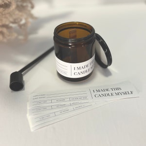 Peut inclure: Un bocal en verre brun pour bougie avec un couvercle noir et une mèche en bois. Le bocal porte une étiquette blanche sur laquelle est inscrit "J'AI FAIT CETTE BOUGIE MOI-MÊME". Il y a également plusieurs étiquettes vierges avec le texte "NOM DE LA BOUGIE:", "NOTES DE PARFUM:", "4 OZ / 125G", "20 HEURES" et "CIRE DE SOJA DORÉE".