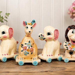 May include: Four vintage ceramic animal figurines on wheels. The collection includes an elephant, a kangaroo, and a lion, each holding a bouquet of flowers. The figurines are painted in pastel colors with blue wheels.