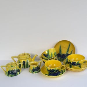 May include: A yellow tea set featuring a hand-painted dark blue iris flower and green leaf motif. The set includes a teapot with a lid, a sugar bowl with a lid, a creamer, three teacups, three saucers, and one additional decorative saucer.
