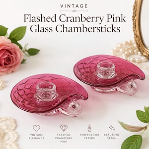 May include: Two cranberry pink glass chambersticks with a clear glass candle holder. The chambersticks have a diamond pattern and a clear glass handle. The text on the image says "VINTAGE Flashed Cranberry Pink Glass Chambersticks."