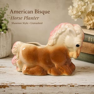 May include: A ceramic horse-shaped planter featuring a glossy finish with a brown body, cream-coloured face, and pink accents on the mane and tail. The text American Bisque Horse Planter Shawnee Style Unmarked is visible above the object.