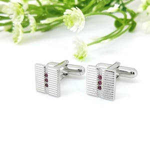 May include: Silver cufflinks with a textured design and three small red gemstones.