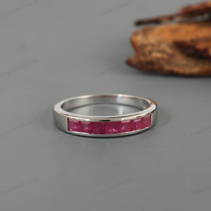 Puede incluir: Un anillo de banda de plata con una fila de piedras de rubí rojo engastadas en un engaste de canal.