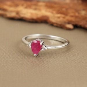 Peut inclure: Une bague de fiançailles en argent avec un rubis en forme de poire et deux petits diamants de chaque côté du rubis.