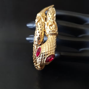 Peut inclure: Un bracelet serpent en or avec des accents de strass rouges. Le bracelet est fait d'écailles de serpent entrelacées.