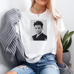 May include: A white t-shirt with a black and white photo of a man with dark hair and a black shirt.